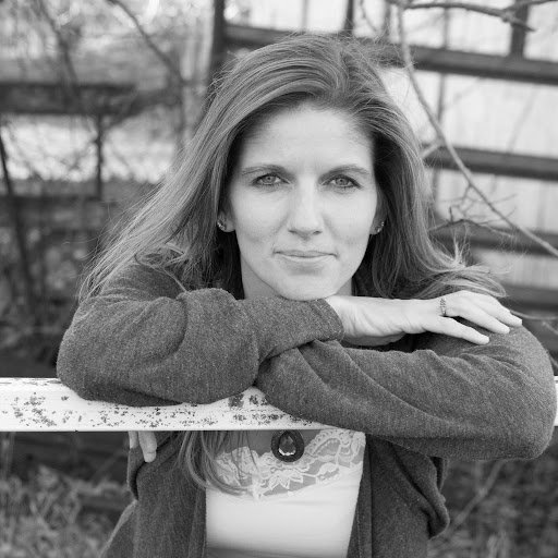 A black and white photo of Kim Braungardt. She is smiling and leaning on a fence railing.