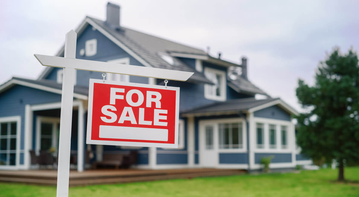 A blue and white two-story home sits behind a red "For Sale" real estate sign.